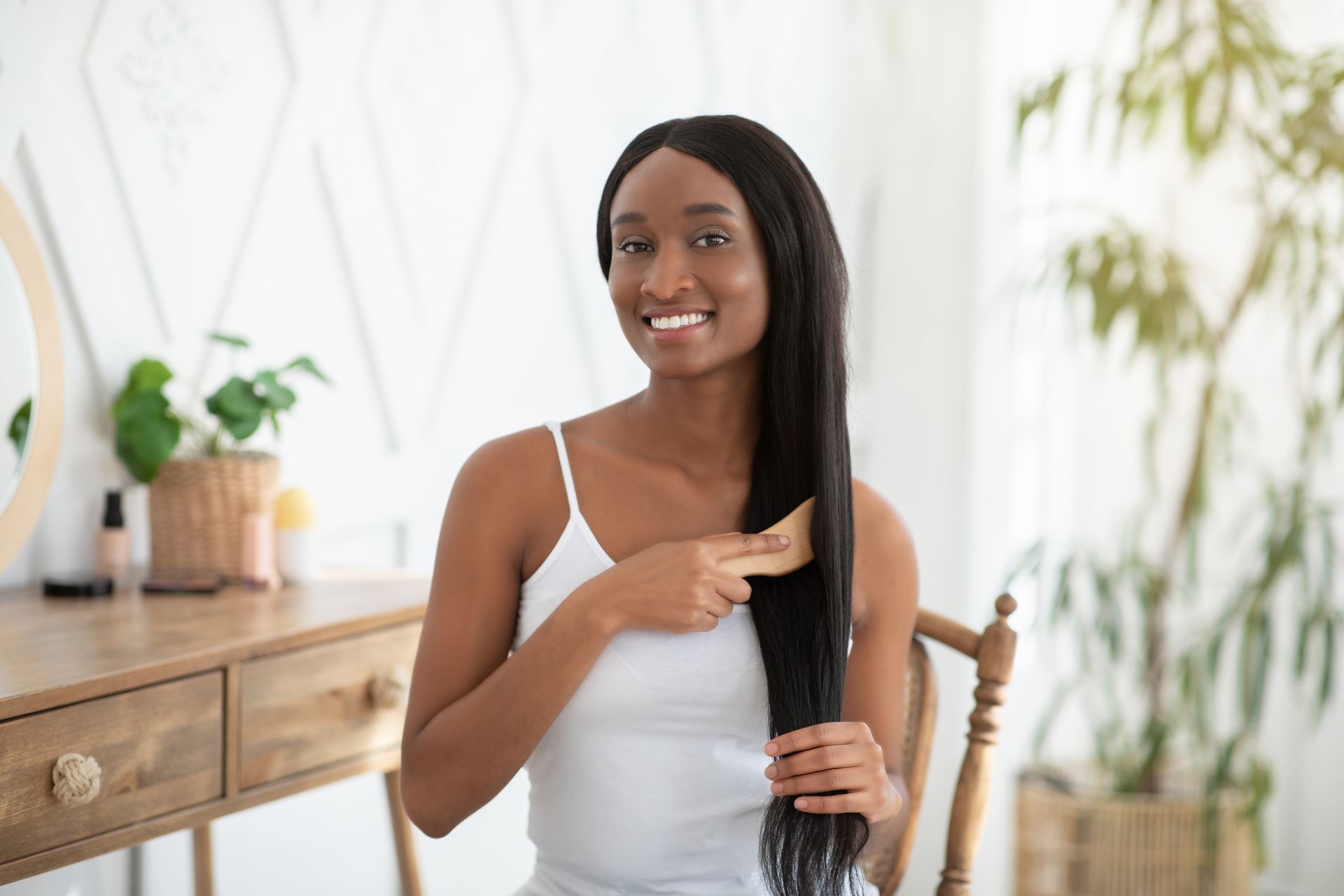 A woman is brushing her hair while sitting in a chair in front of a mirror.