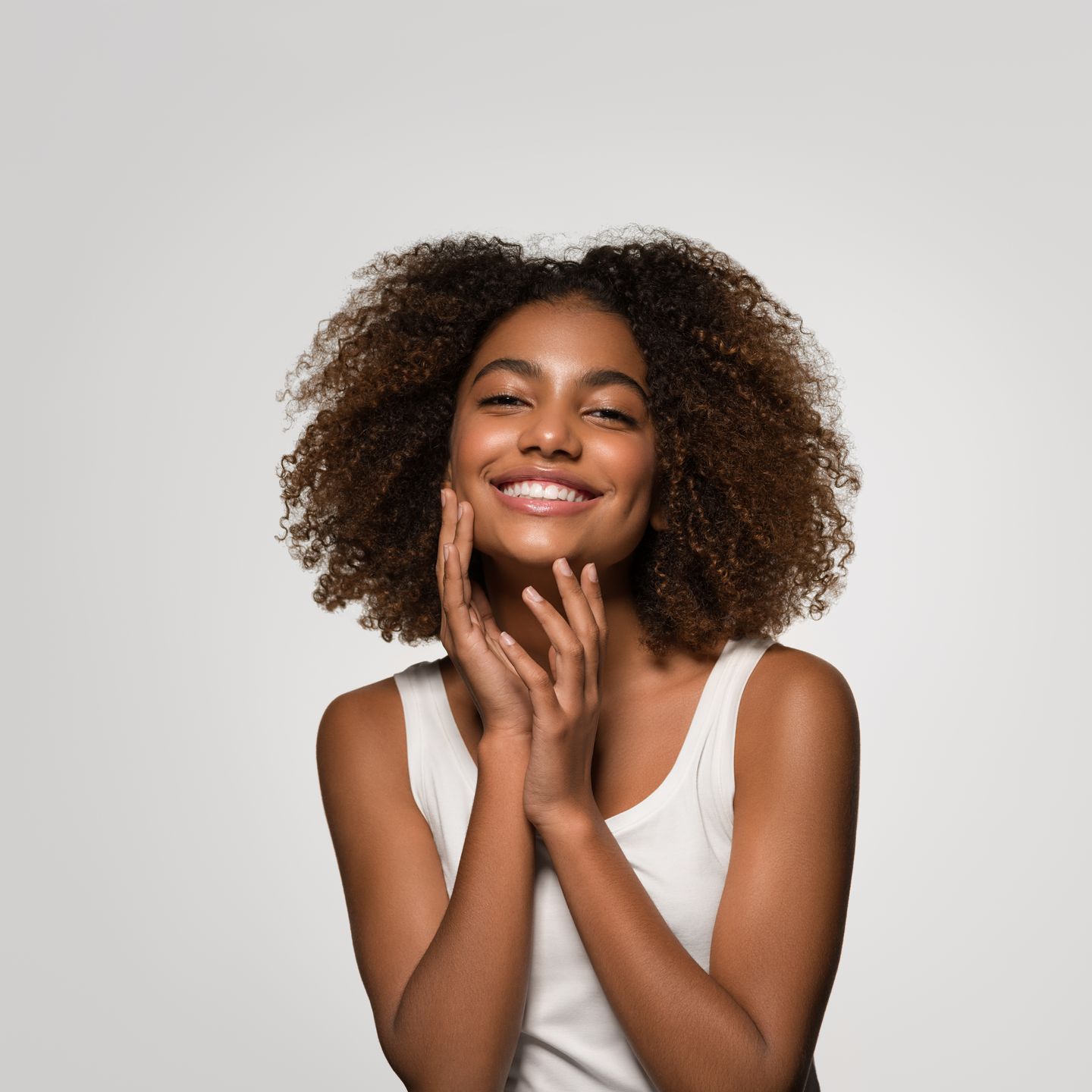 A woman with an afro is smiling and touching her face.
