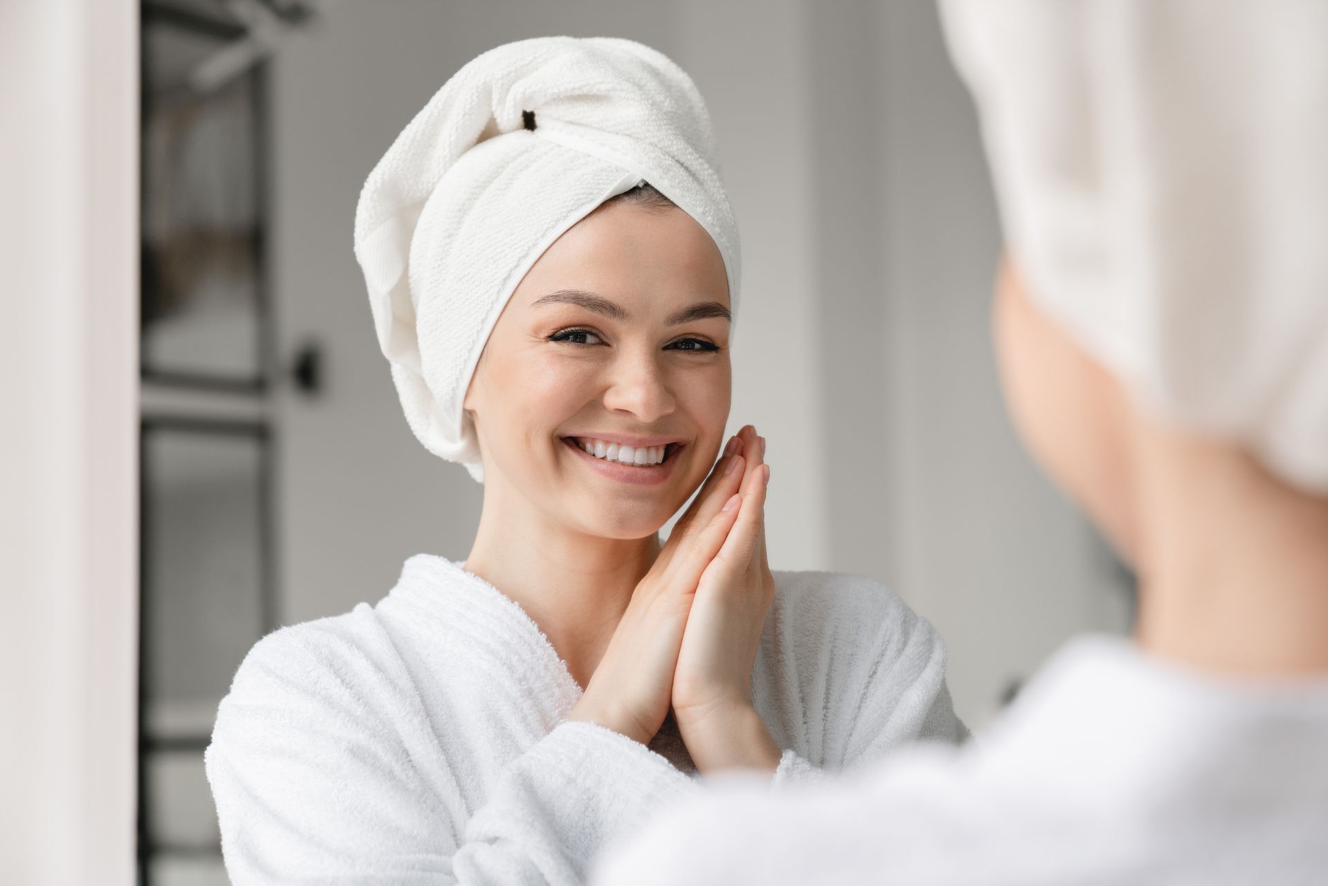 A woman with a towel wrapped around her head is smiling in front of a mirror.