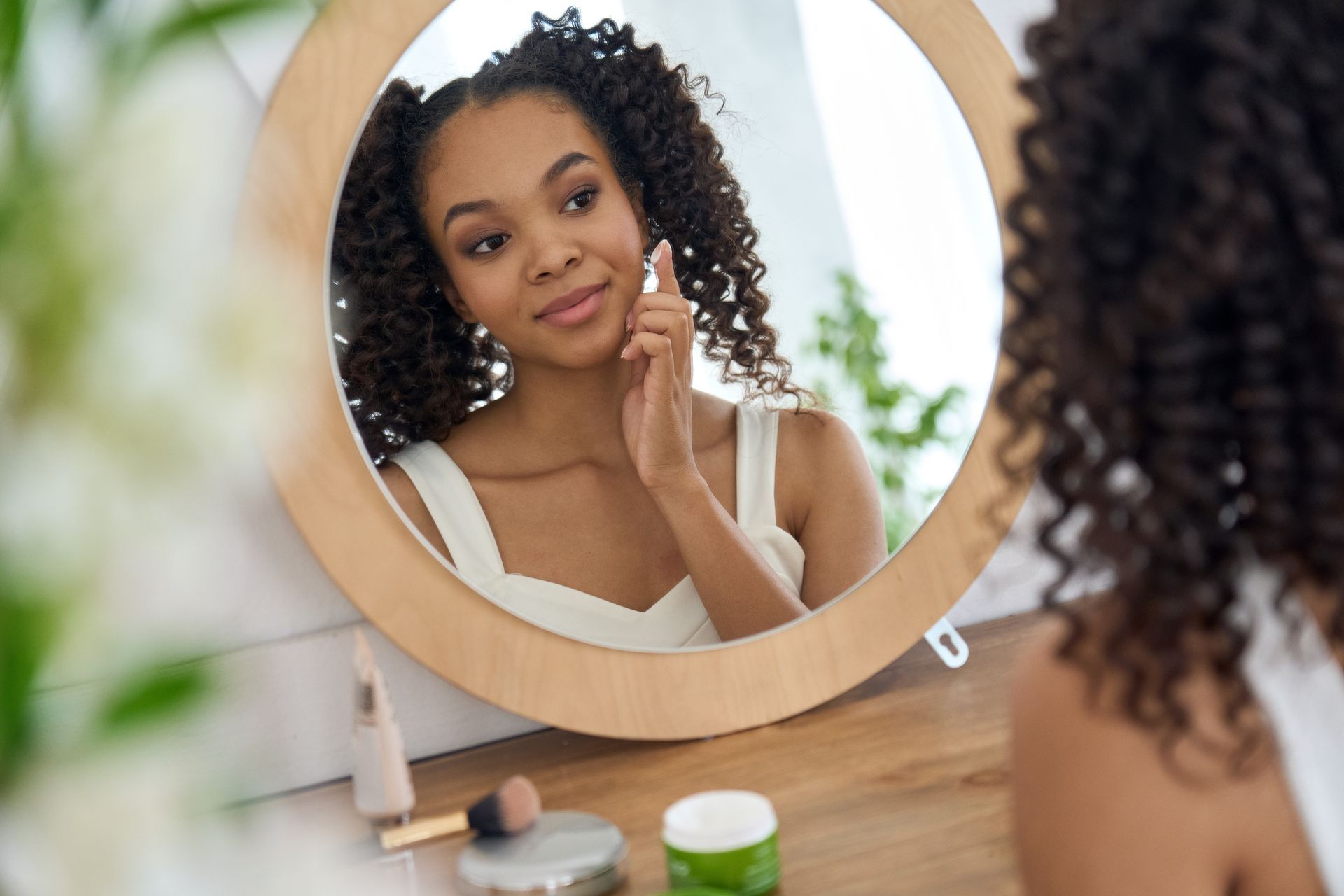 A woman is looking at her face in a mirror.