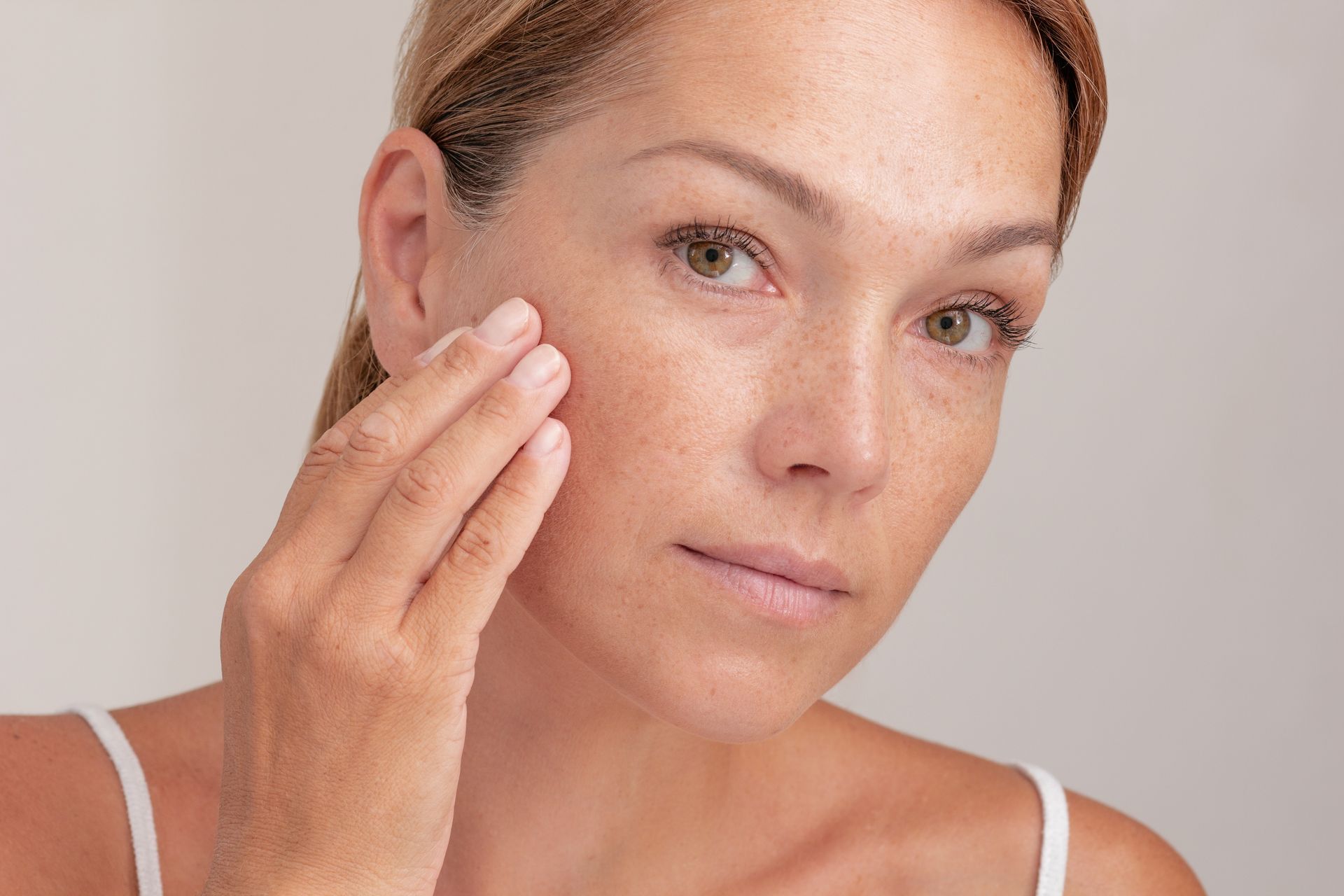 A woman is applying lotion to her face.