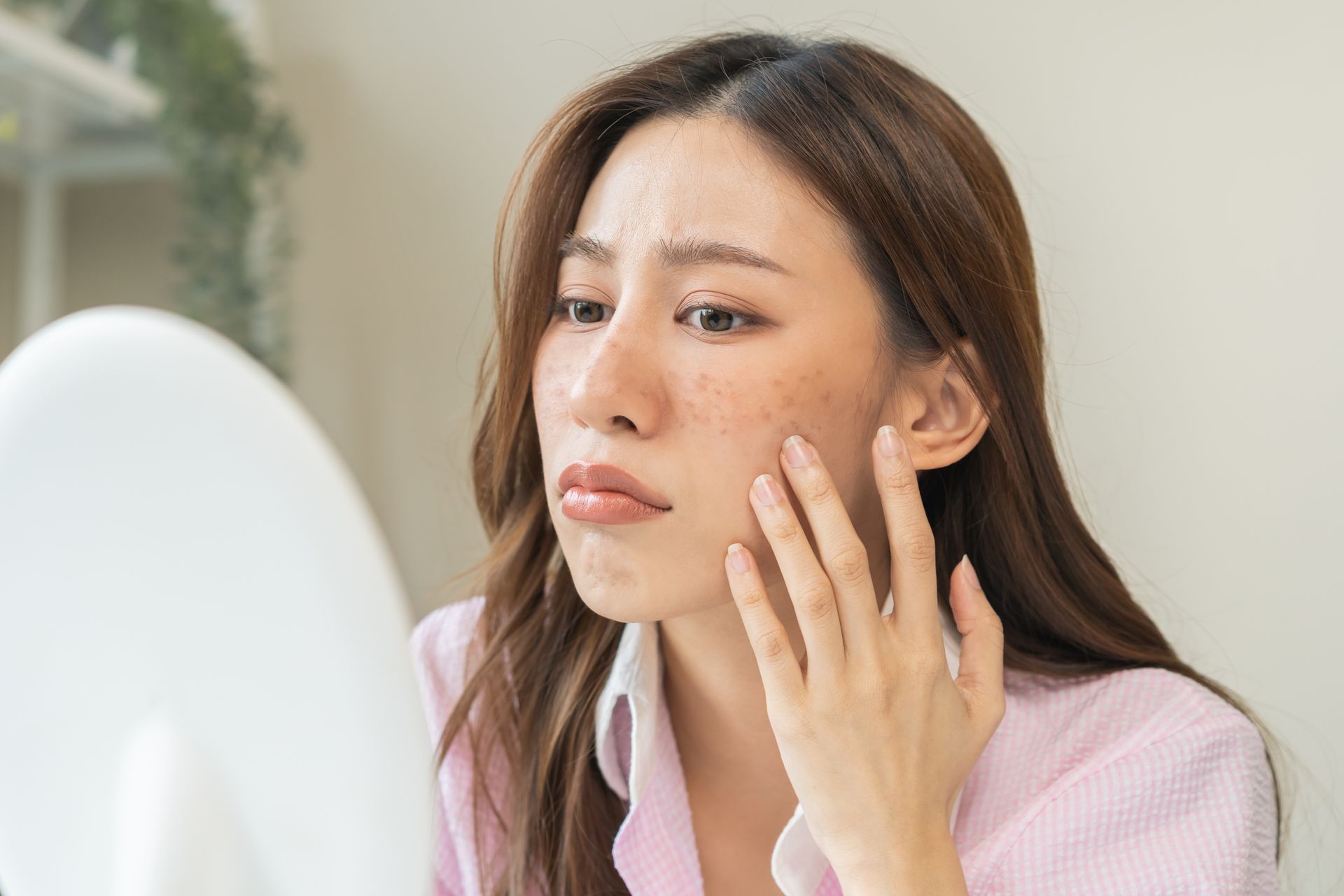 A woman is looking at her face in a mirror.