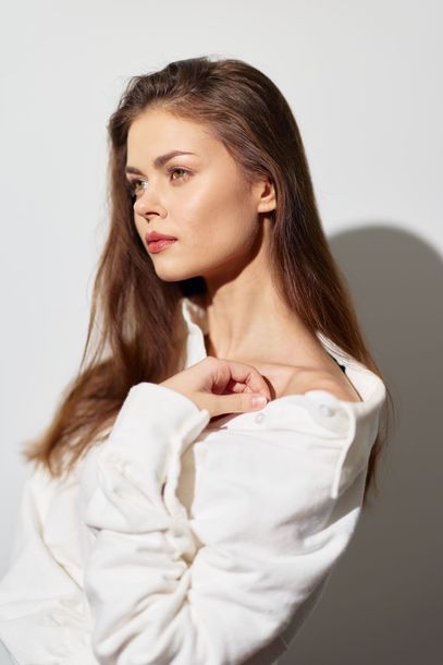 A woman in a white sweater is standing in front of a white wall.