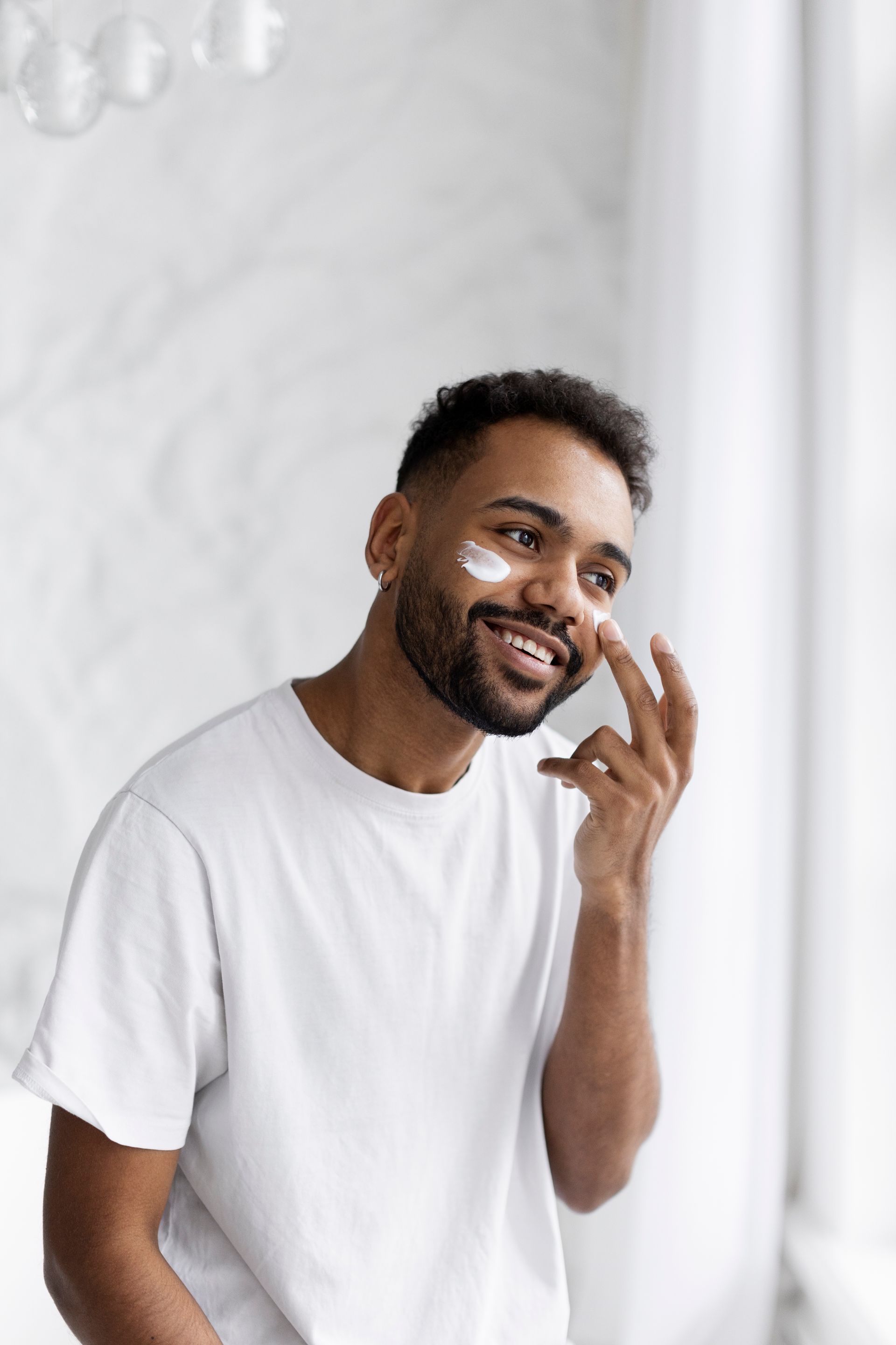 A man is applying cream to his face in front of a mirror.