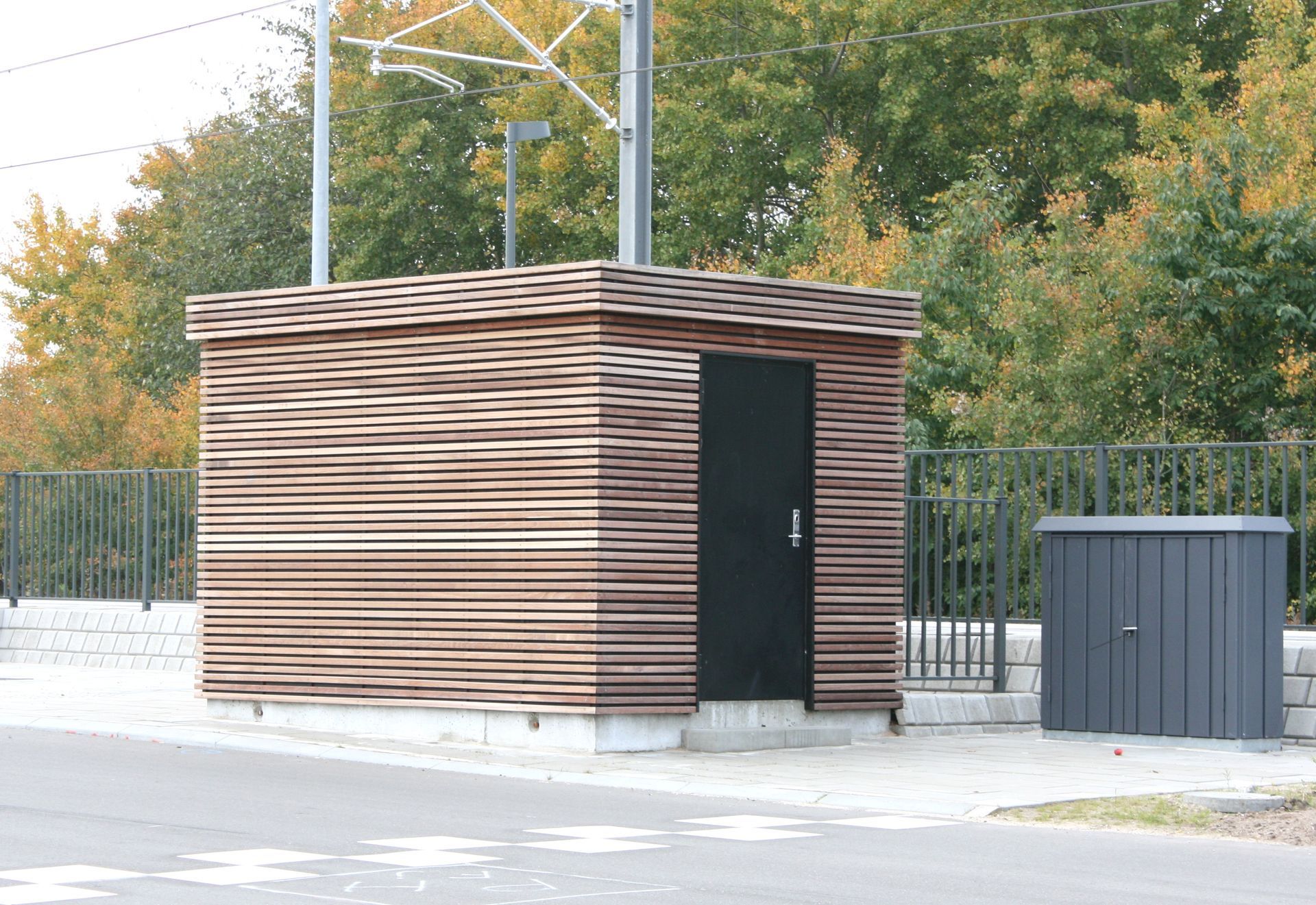 En lille træbygning med en sort dør og et hegn i baggrunden