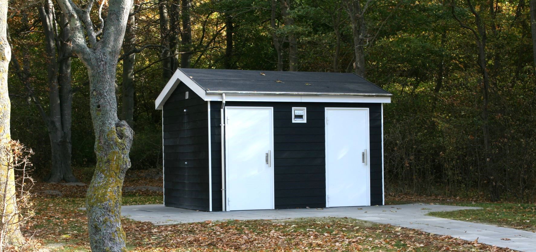 Et sort skur med to hvide døre midt i en skov