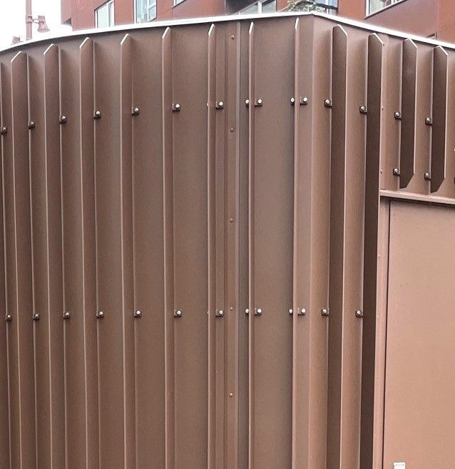 Et brunt hegn med en murstensbygning i baggrunden