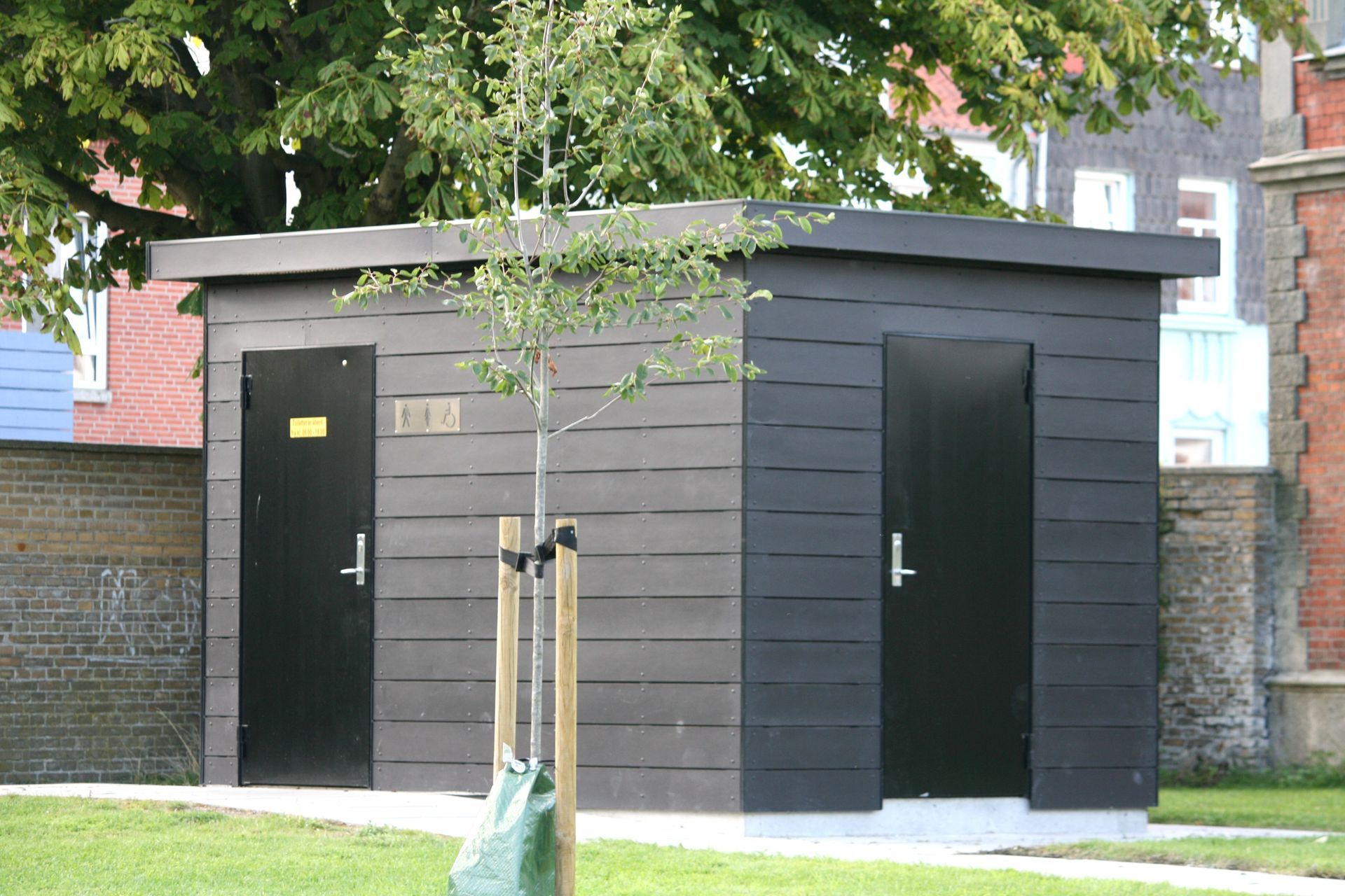 En lille bygning med to døre og et træ foran