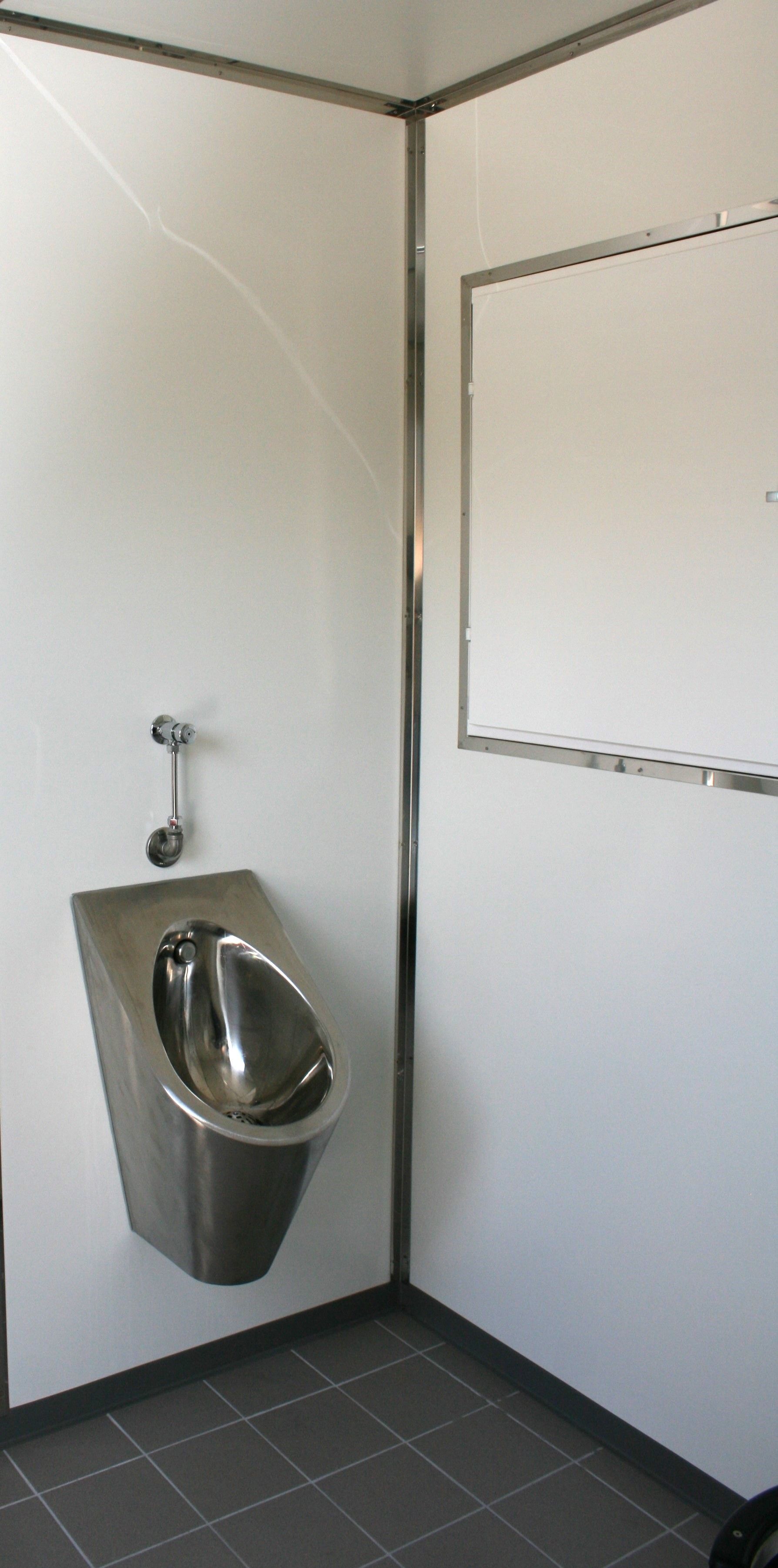 Et urinal i rustfrit stål hænger på en hvid væg i et badeværelse.