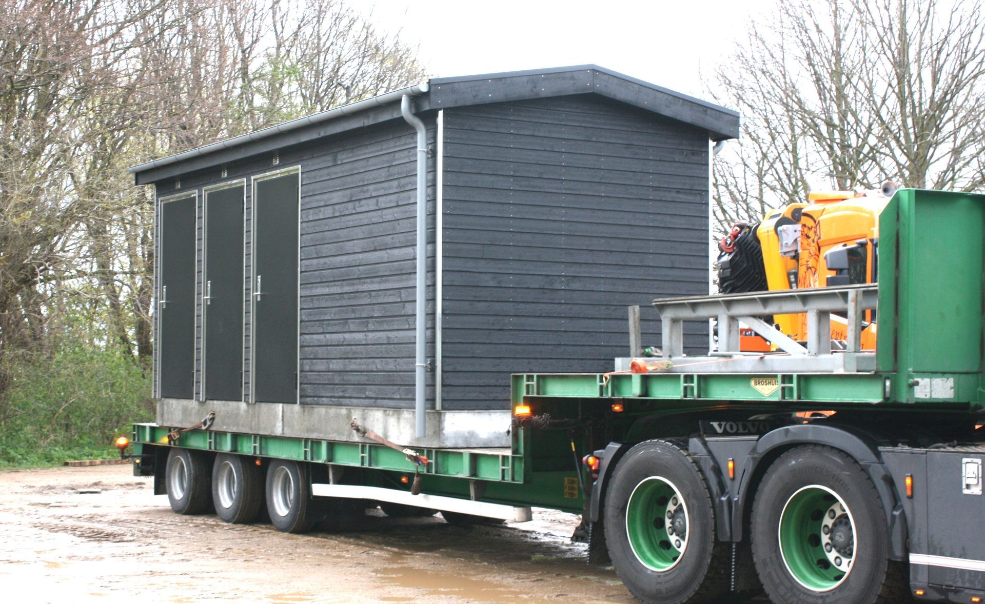 En grøn semi lastbil transporterer en lille bygning