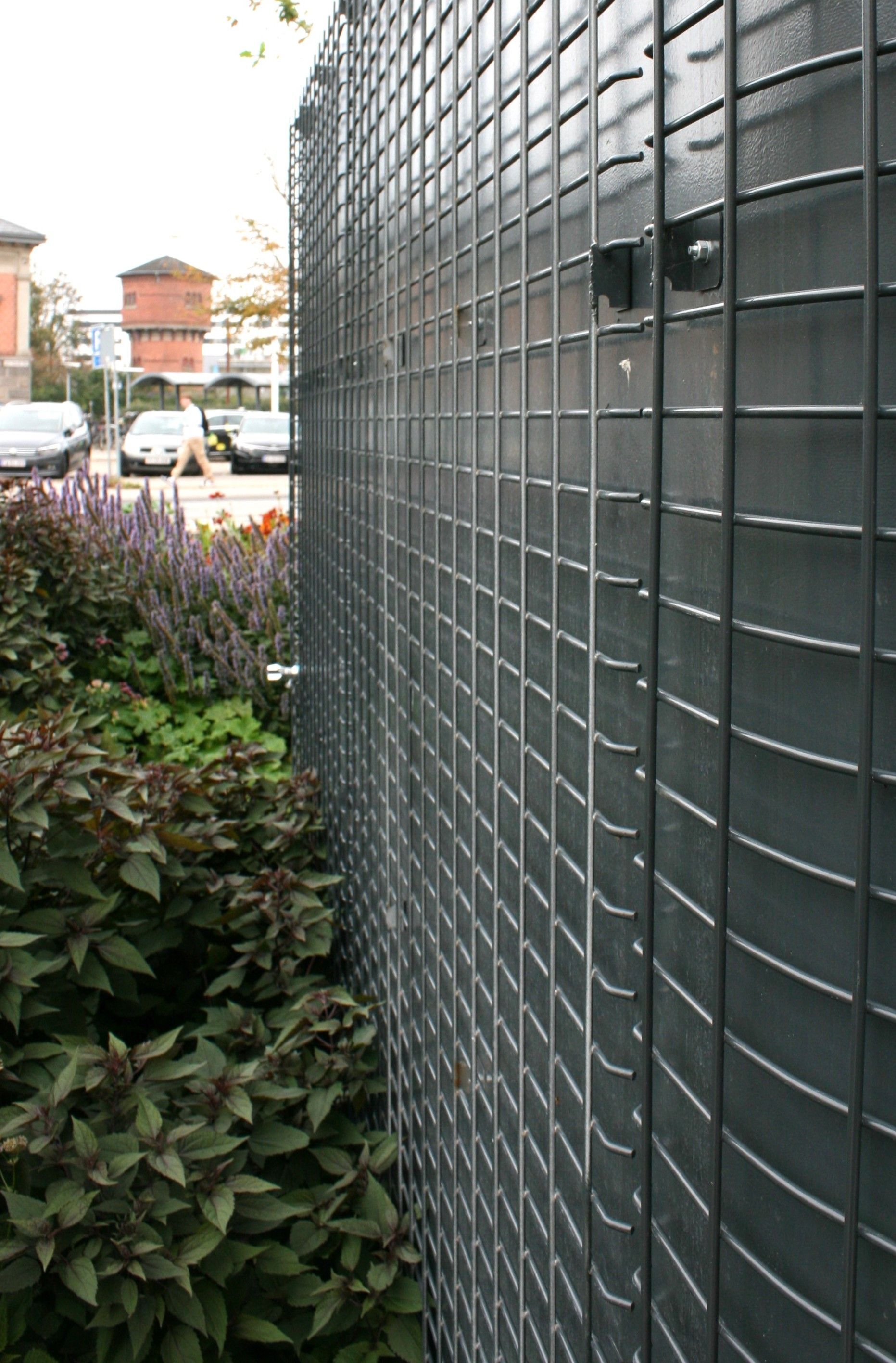 Et nærbillede af et metalhegn med planter i baggrunden.