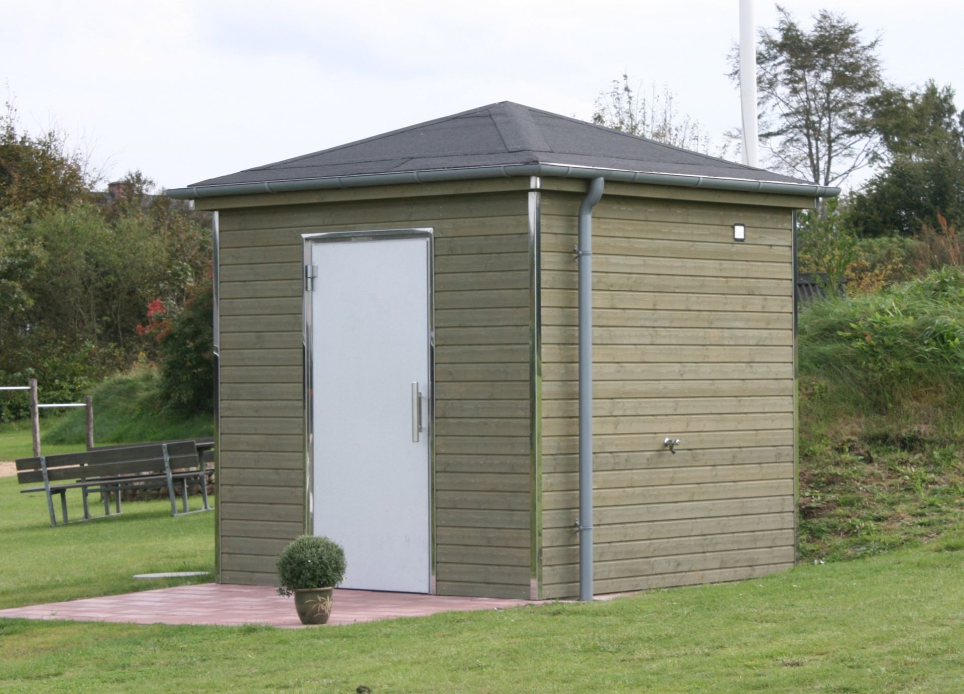 Et lille skur med hvid dør og en potteplante foran