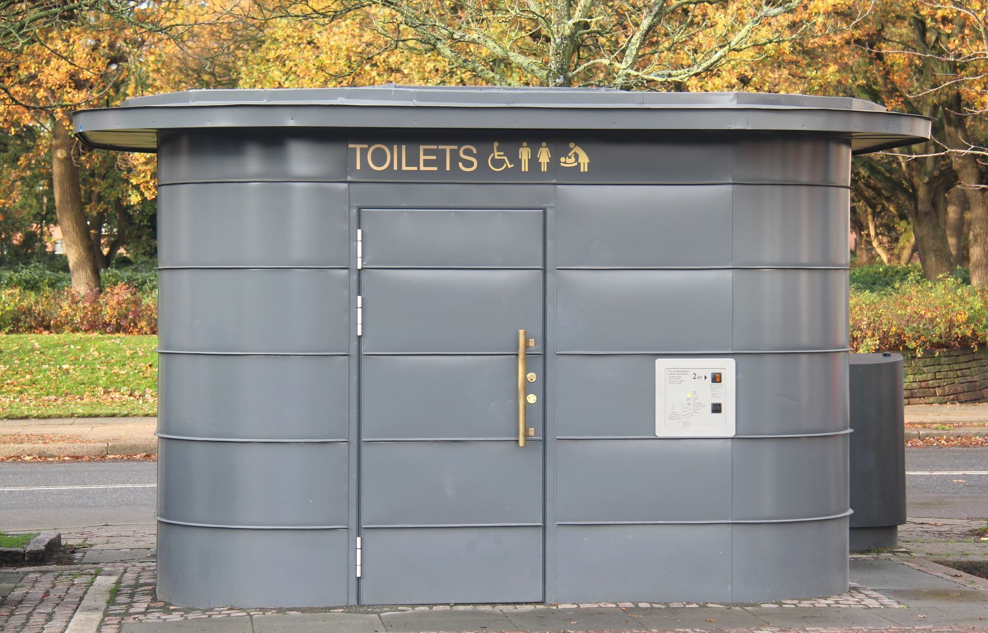 En lille grå bygning, hvor der står toiletter på