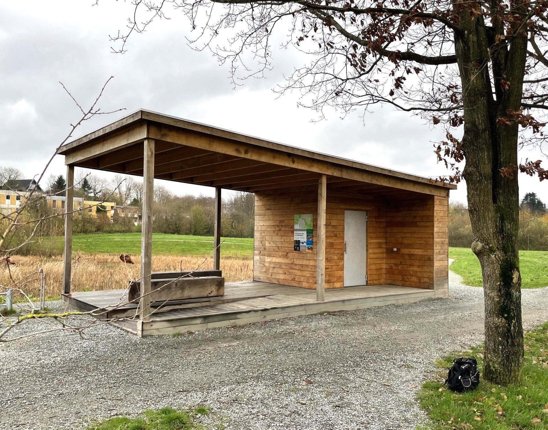 En lille træbygning med en veranda og et træ i baggrunden