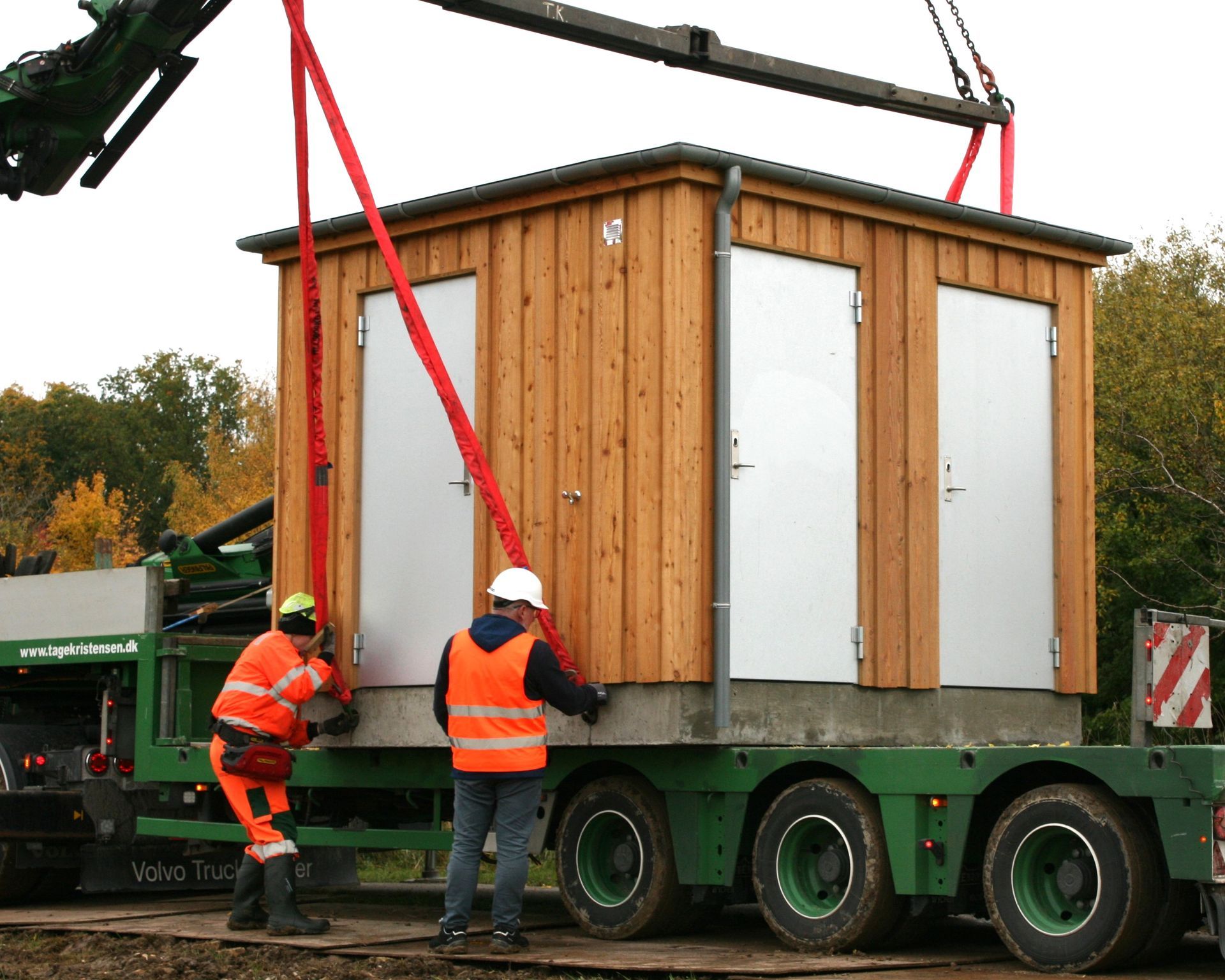 En kran løfter en træbygning på en trailer