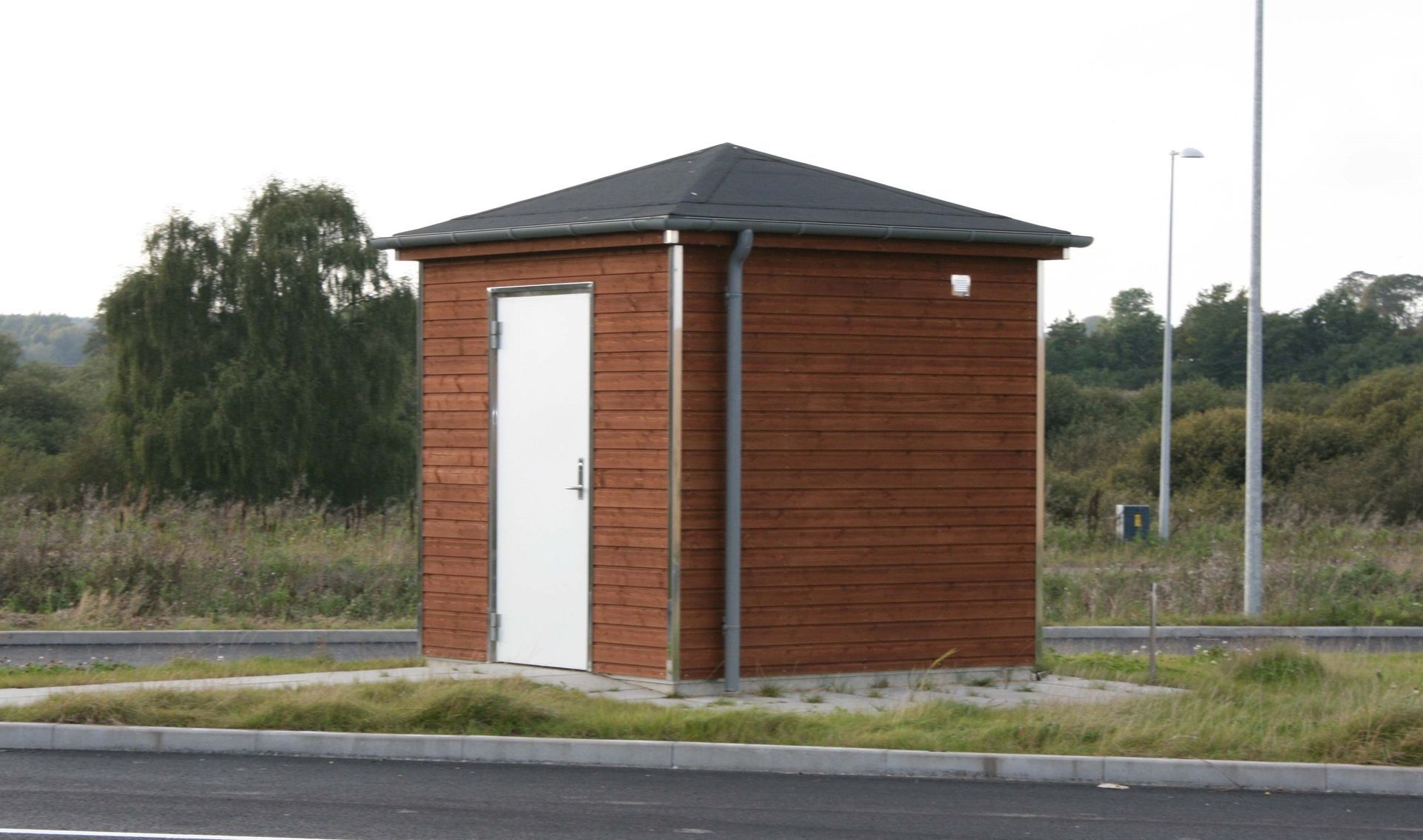 En lille træbygning med hvid dør og sort tag