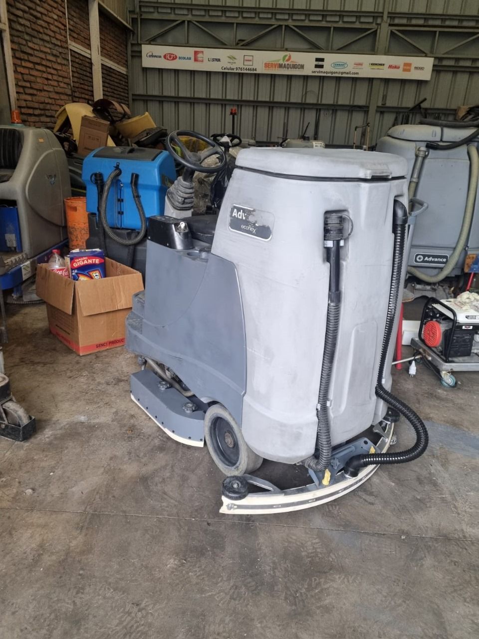 Maquina limpiadora de suelos en almacén, con componentes grises y negros.