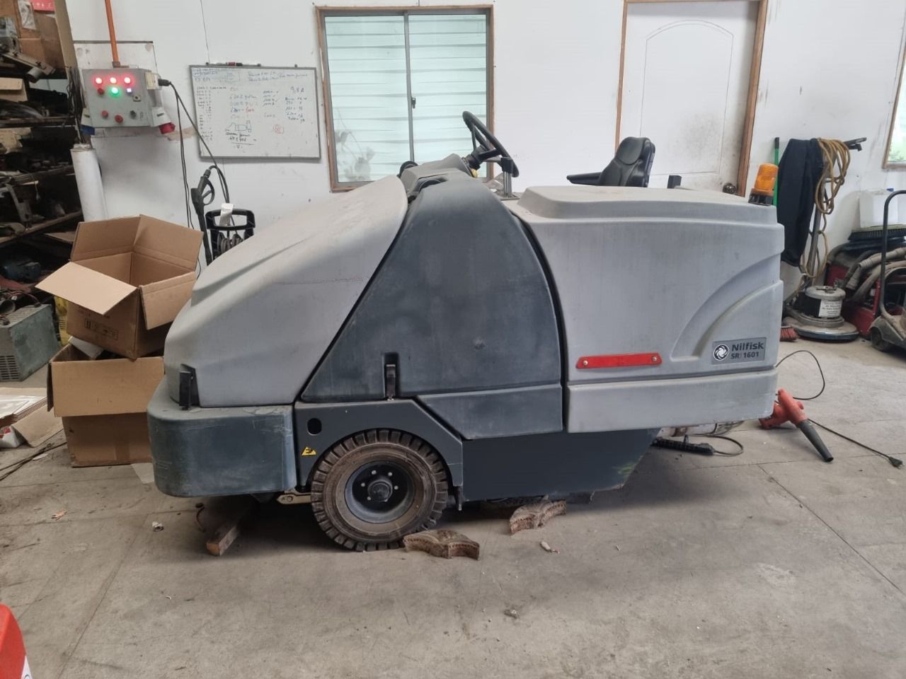 Una barredora gris dentro de un garaje. Tiene un volante pequeño y un asiento.