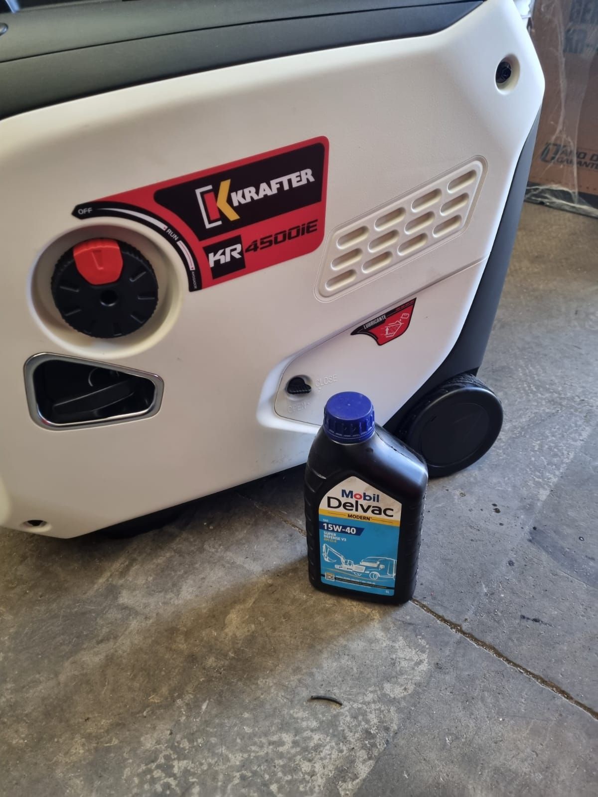 Generador Krafter HR4500IE blanco y negro con una botella de aceite Mobil Delvac sobre un piso de concreto.