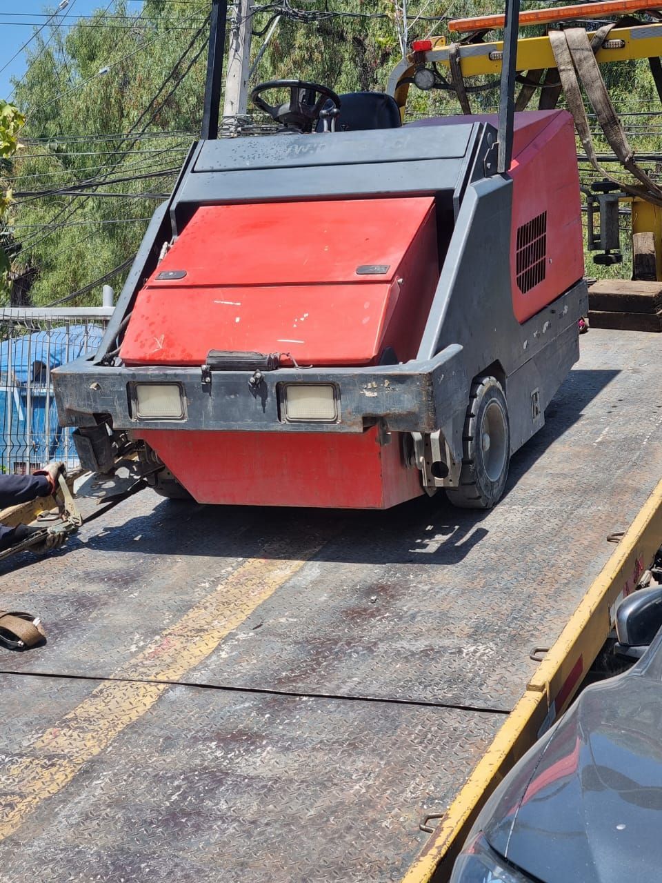 Barredora de calles de color rojo y gris en una rampa, lista para ser transportada.