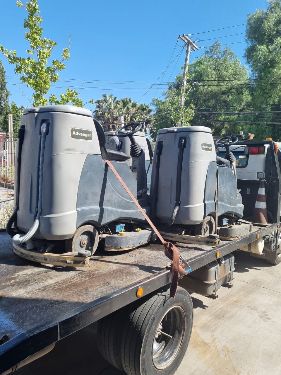 Fregadoras de pisos cargadas en un camión de plataforma, listas para el transporte. Máquinas grises contra un cielo azul.