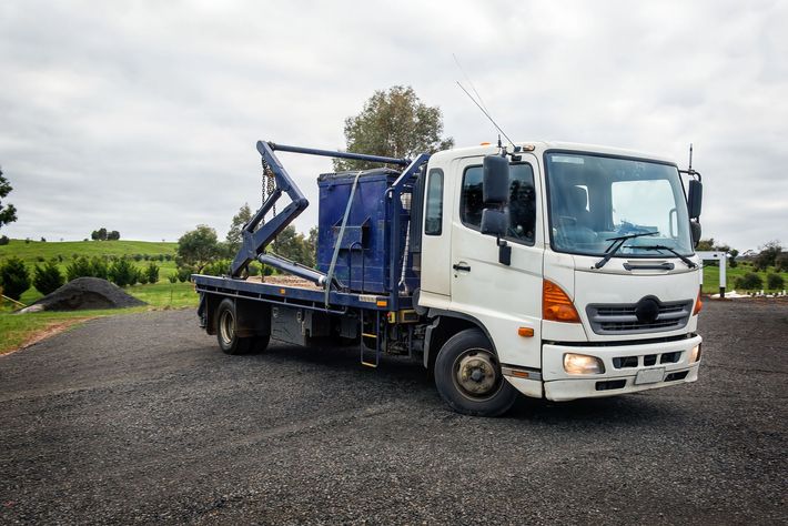 Un camion bianco con un rimorchio blu è parcheggiato in un terreno di ghiaia.