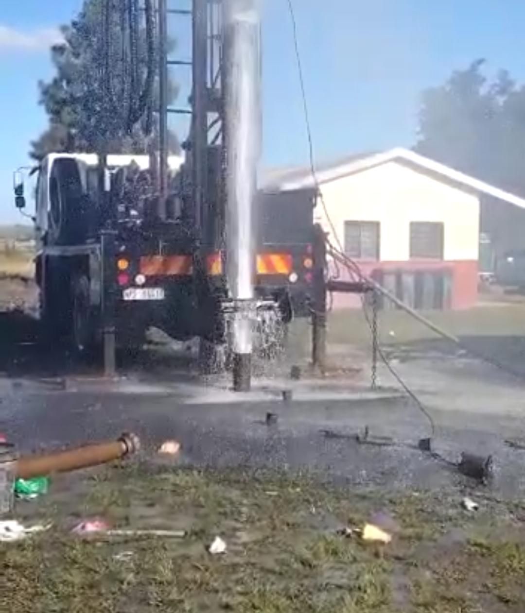 A truck is drilling a hole in the ground in front of a house.