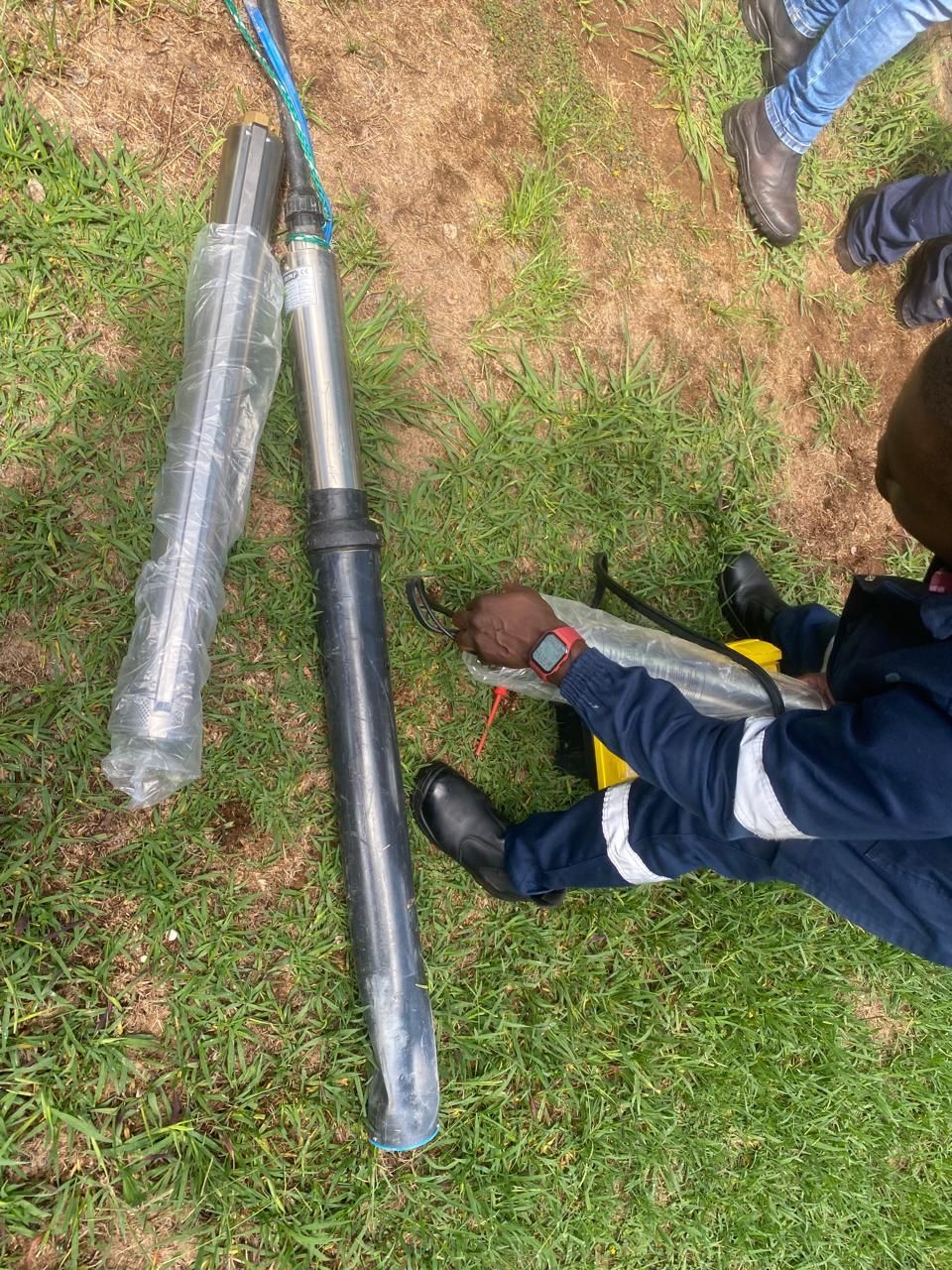 A group of men are working on a borehole pipe in a field.