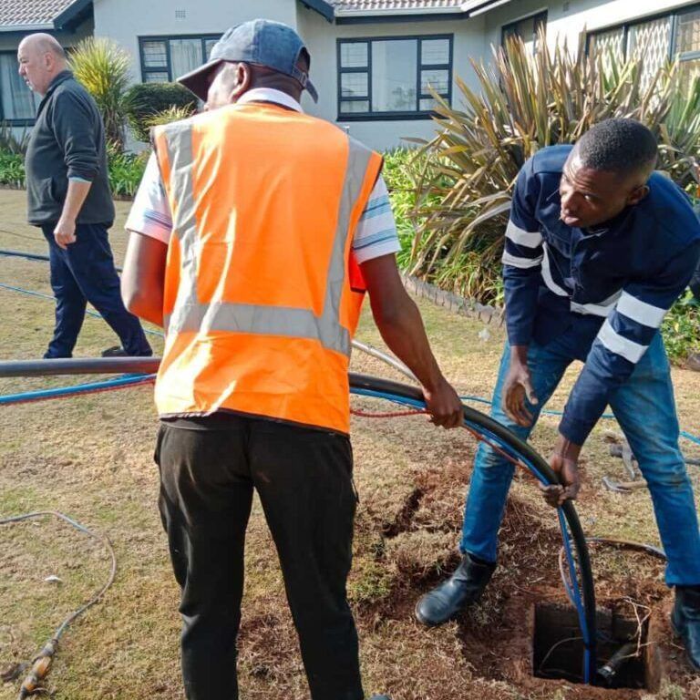 Two men installing a pipe into a borehole opening in the ground
