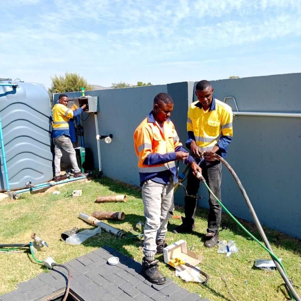 Two men are working on a hose in a yard