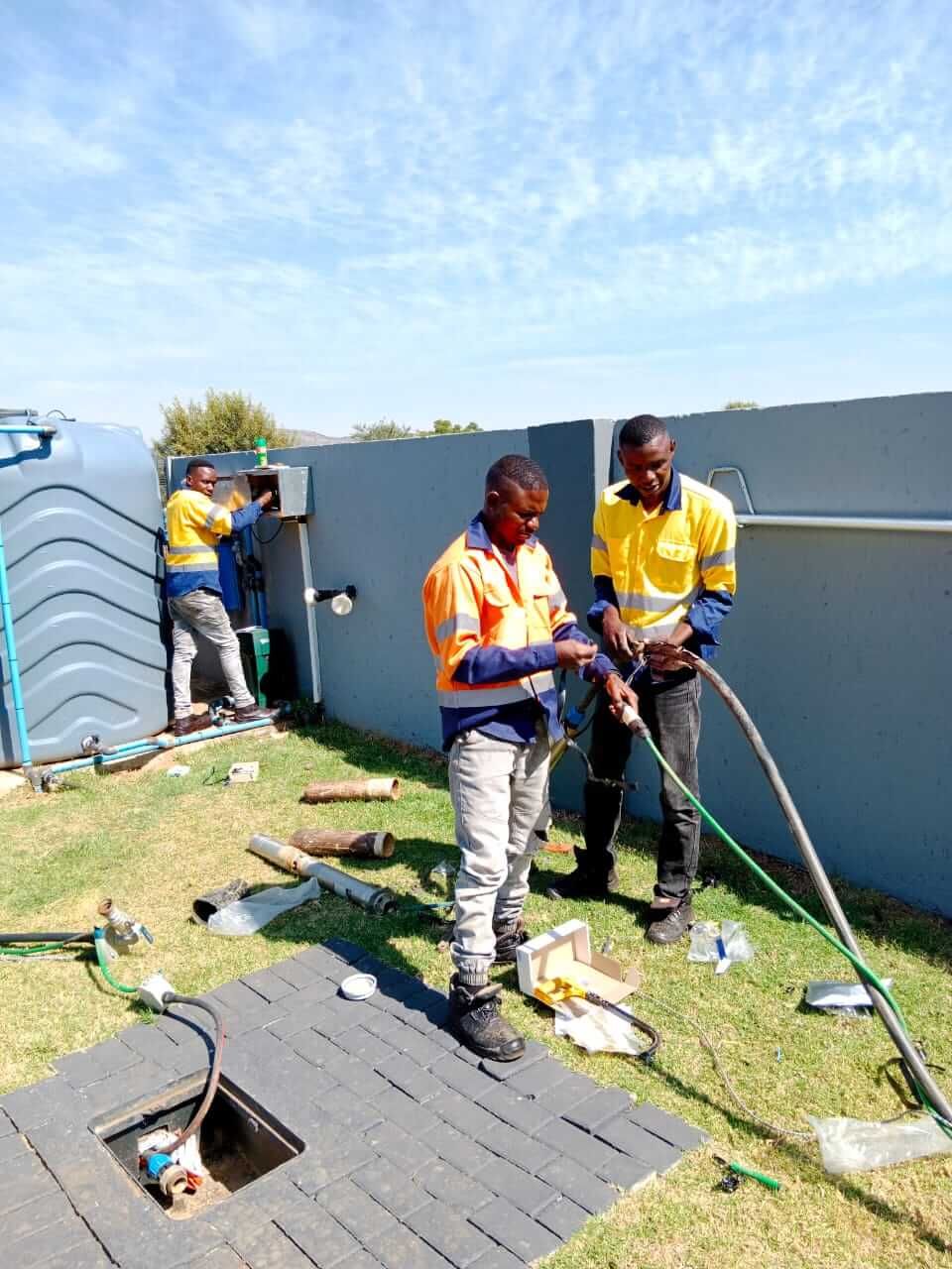 Two men are working on a drain in a backyard.