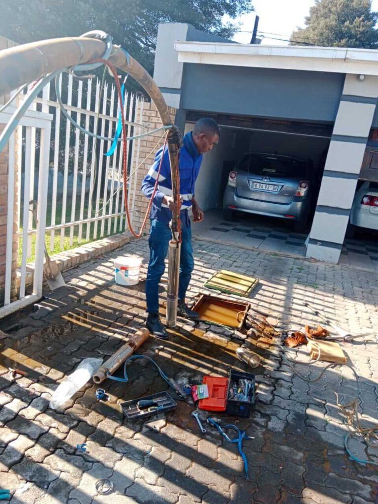 A man is working on a water pump in front of a garage.