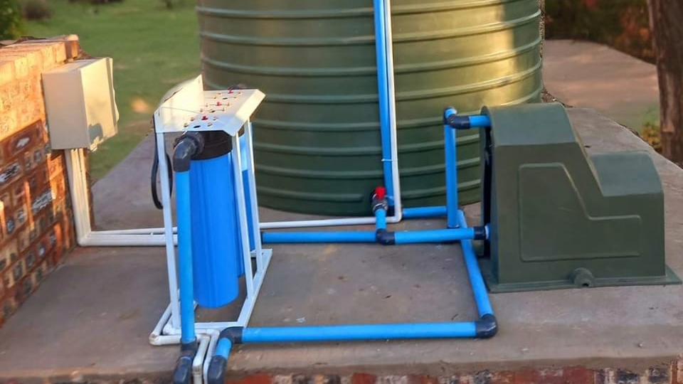 A green water tank is sitting next to a blue pipe.