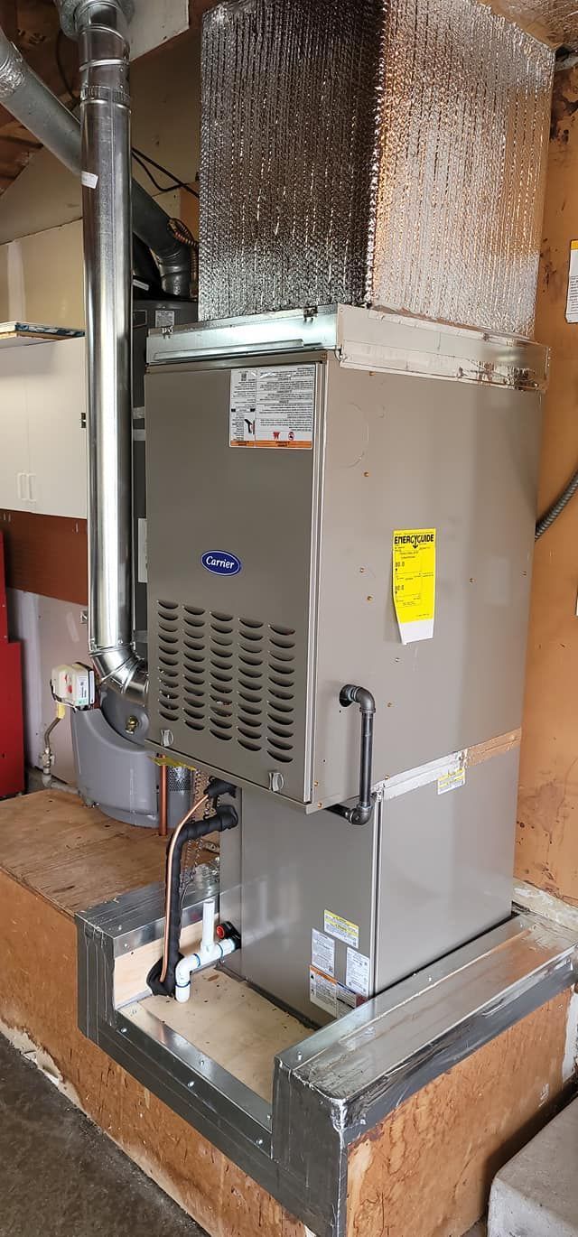 A Carrier furnace installed in a residential setting. It is gray, with a yellow energy efficiency sticker.