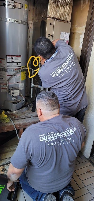 Two people in grey shirts working on a water heater in an enclosed space.