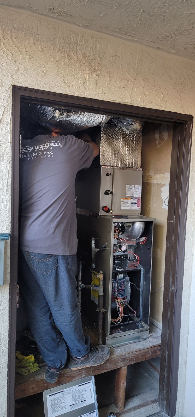 A person working on an HVAC system inside a walled enclosure. They are standing and working on the open unit.