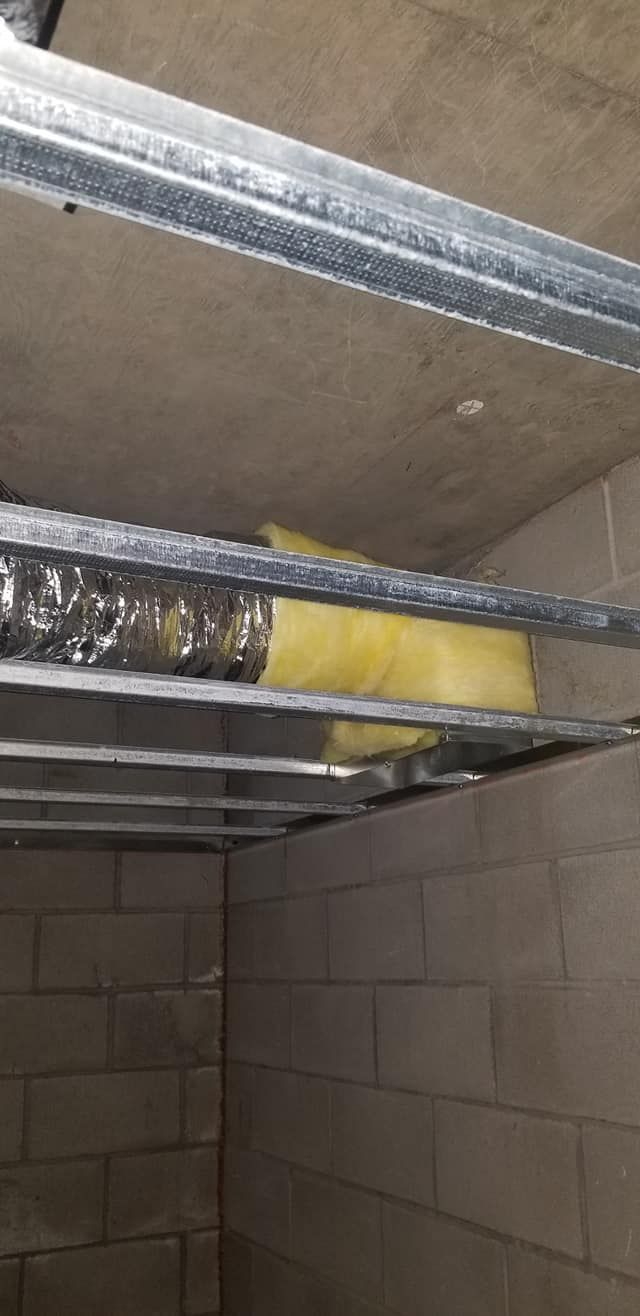 View of ceiling supports and ductwork, with insulation between metal framing. Cinder block wall below.