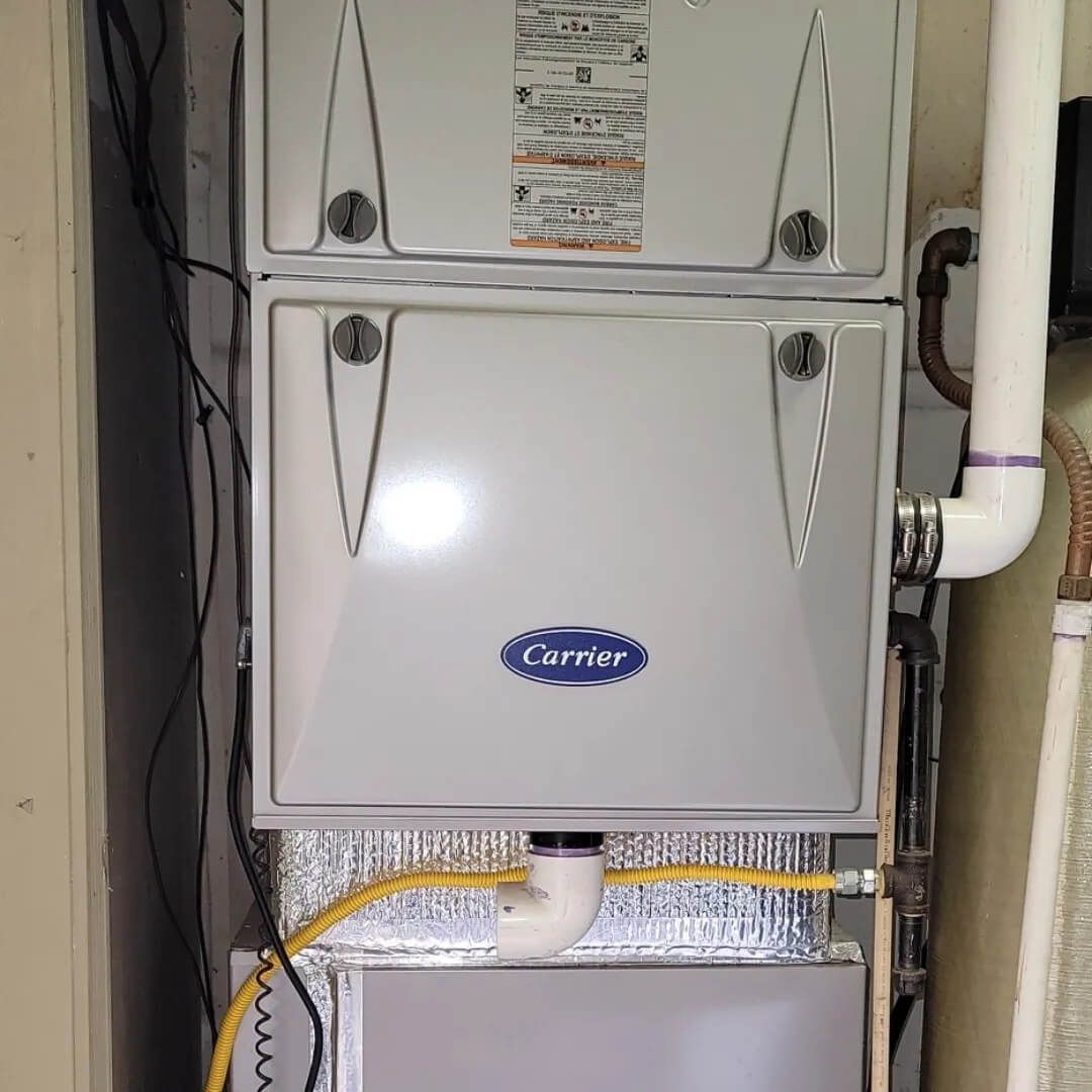 A Carrier furnace with three sections; white metal with blue logo in a utility room.