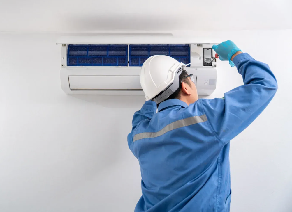 Person in blue gloves using a screwdriver to maintain a white air conditioning unit.