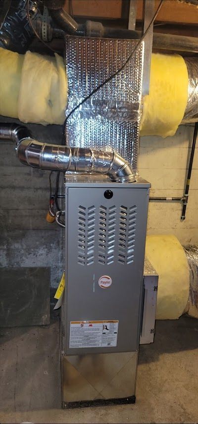 A silver furnace with ductwork in a basement setting.