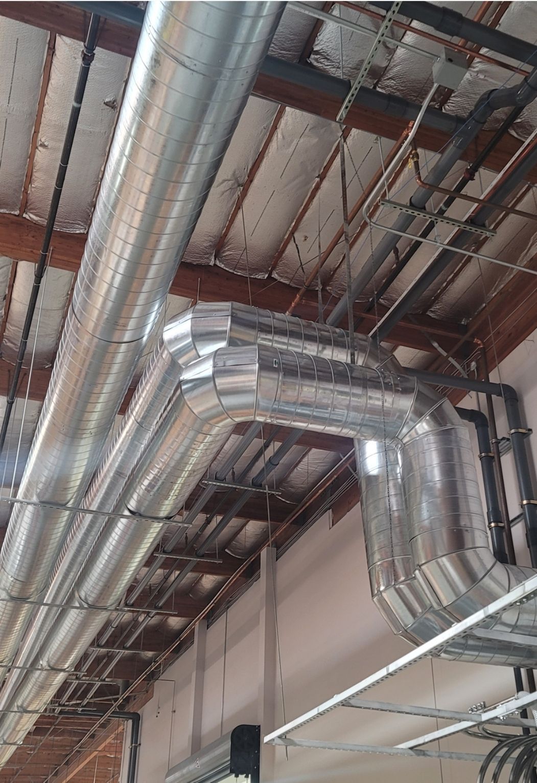 Silver ductwork runs along the ceiling, intersecting with other pipes and supports in an industrial setting.