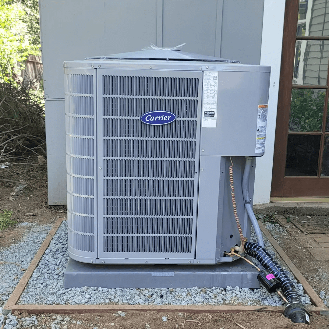 Gray Carrier air conditioning unit on a gravel bed, outside a building.