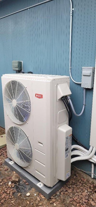 An outdoor HVAC unit on a concrete pad with two fans and electrical connections, set against a blue wall.