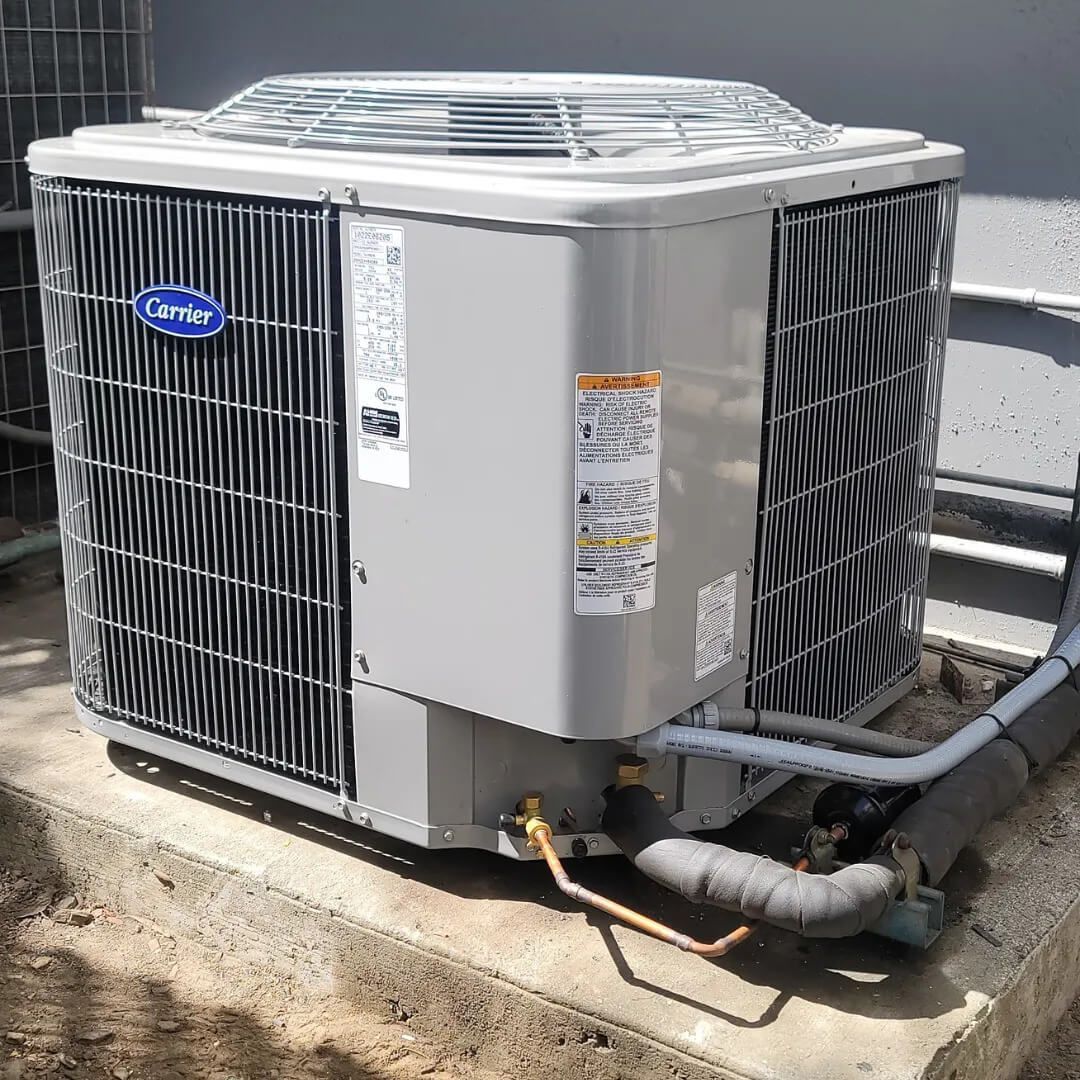 Gray Carrier air conditioning unit on a concrete pad, outdoors.