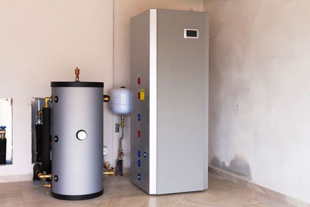 Two large silver tanks, likely for heating, in a room. One tall, one short and round.