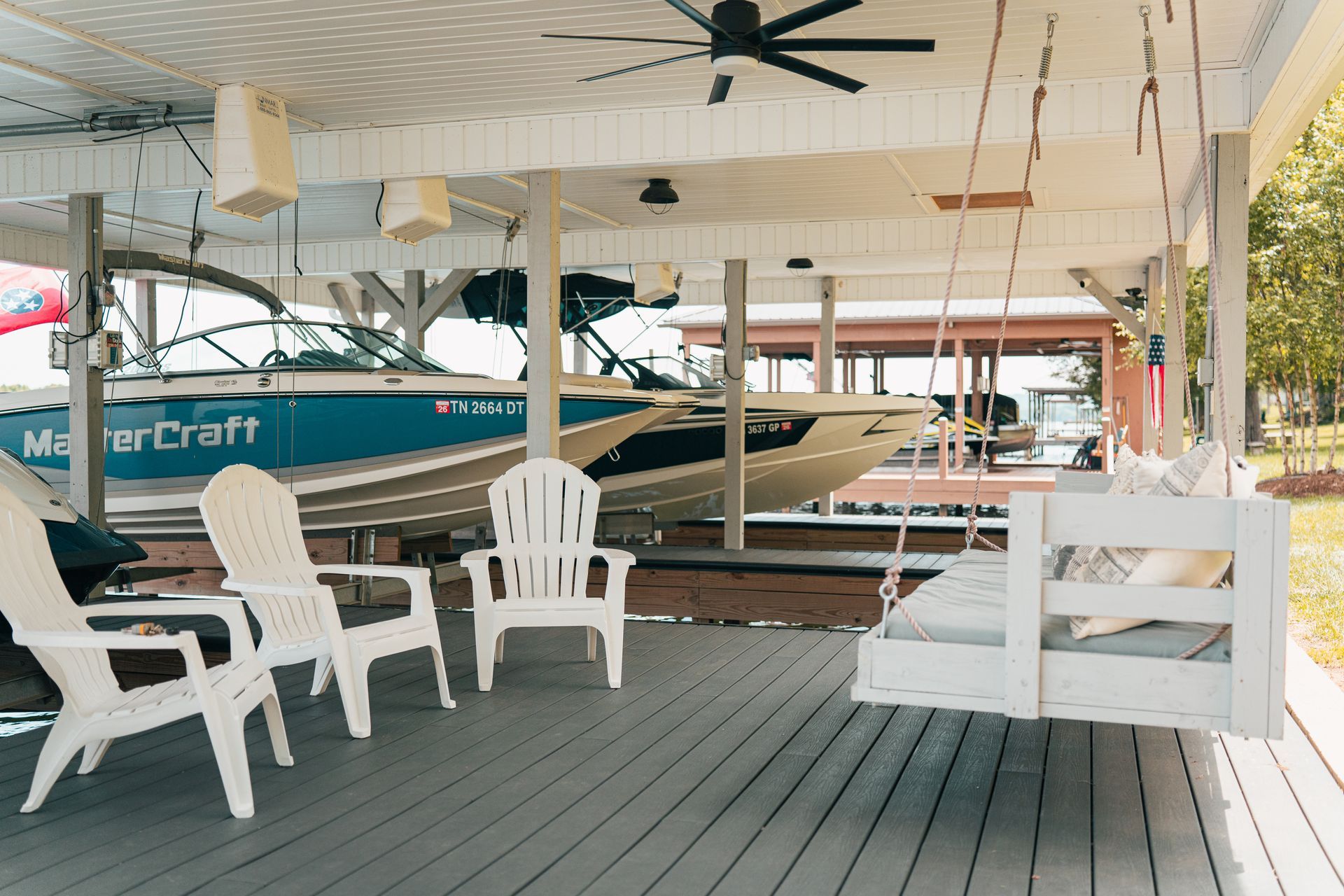 A boat is sitting under a porch with chairs and a swing.