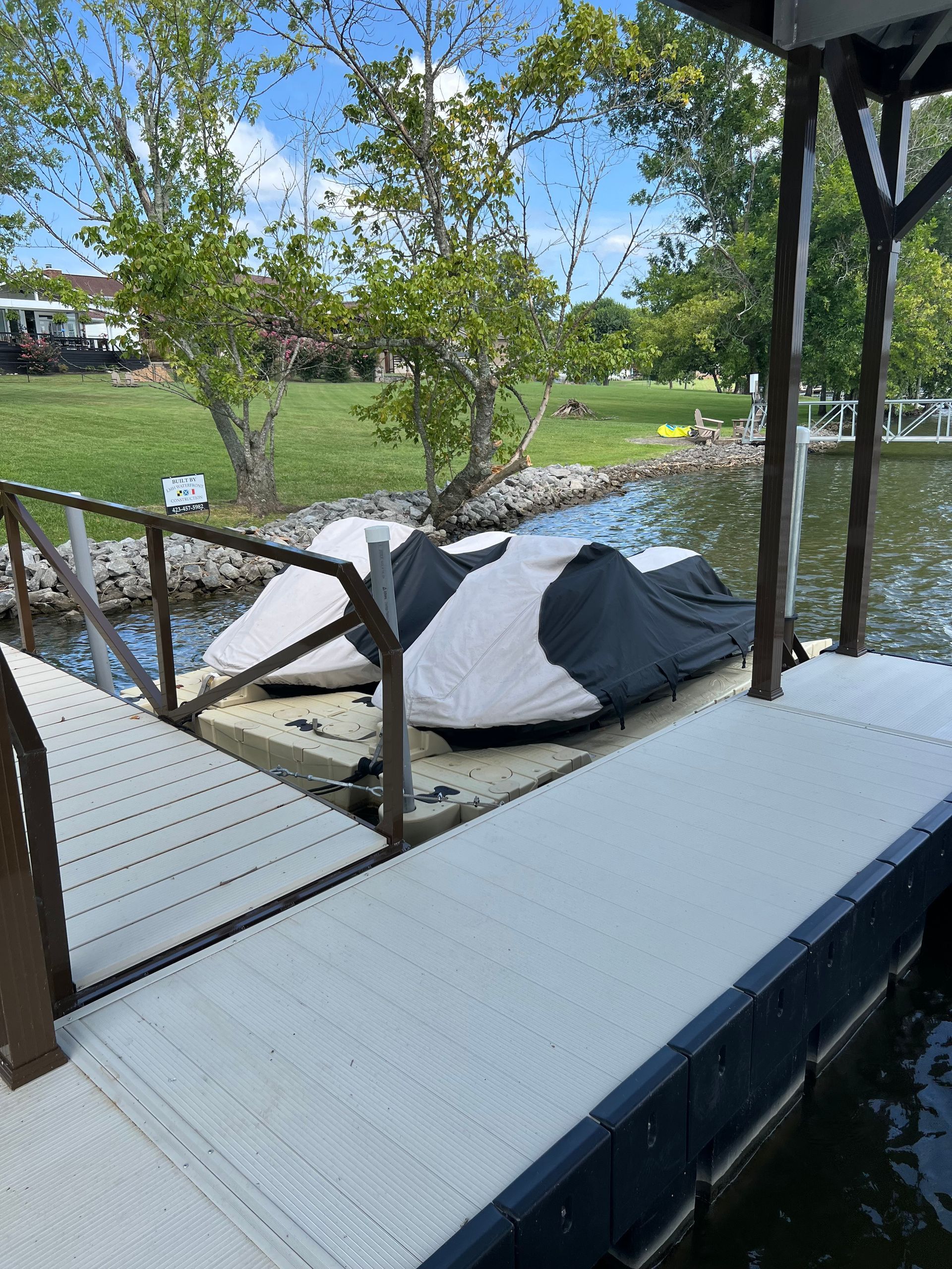 Boat dock with covered boats, overlooking a lake. Sunny day.
