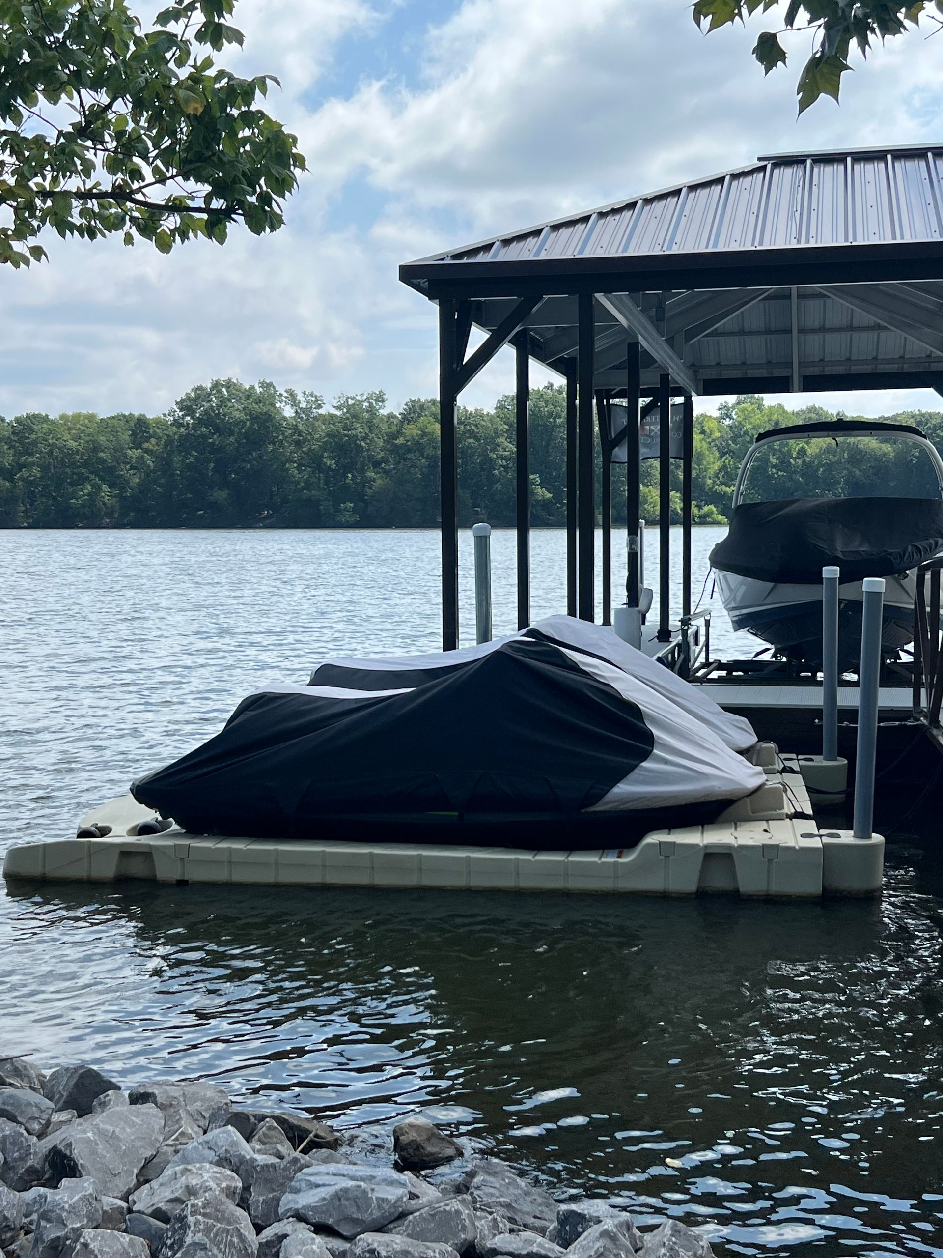 Jet skis and boat covered in a dock with a lake in the background under a cloudy sky.