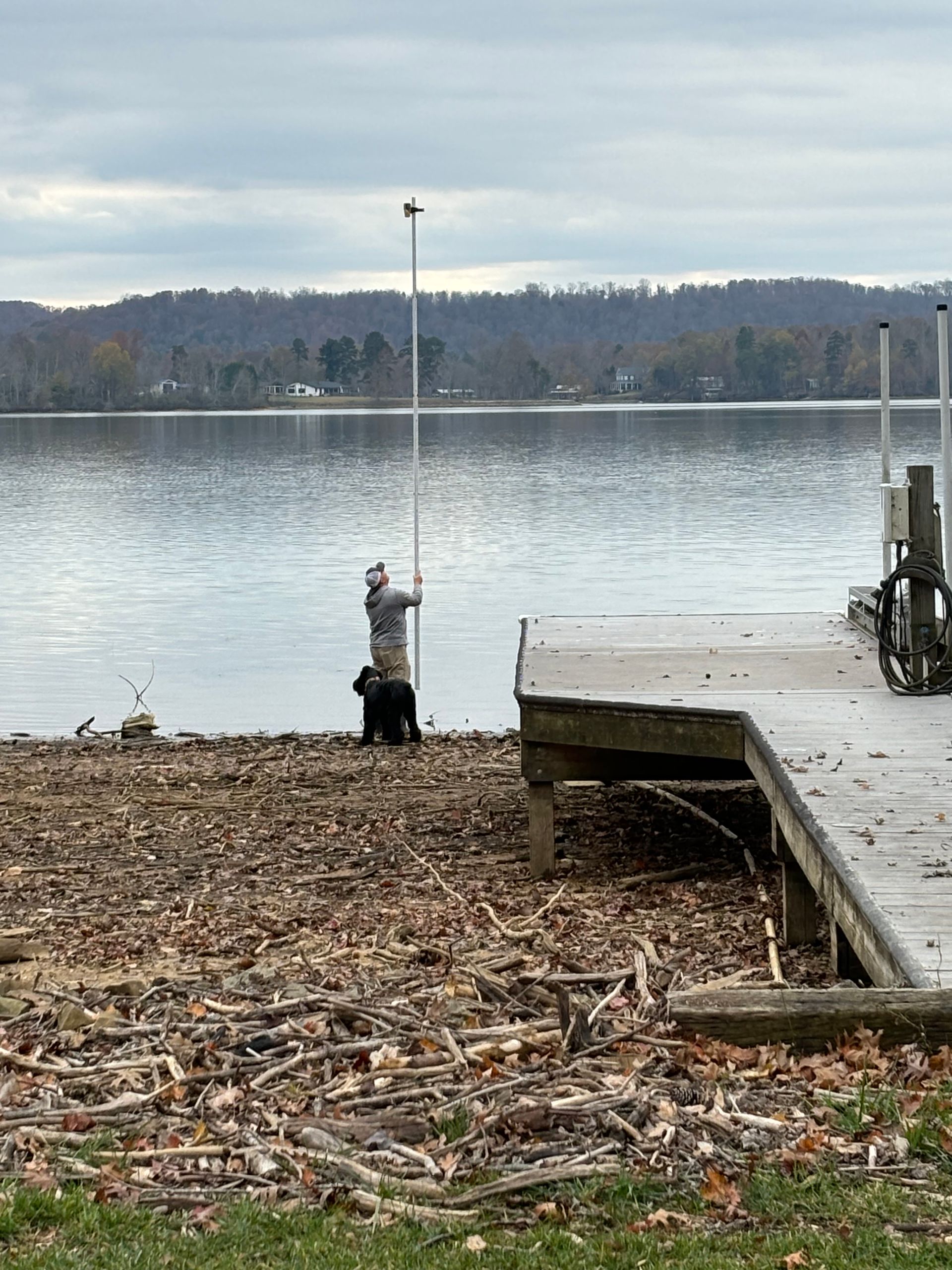 A man and a dog are fishing on the shore of a lake.