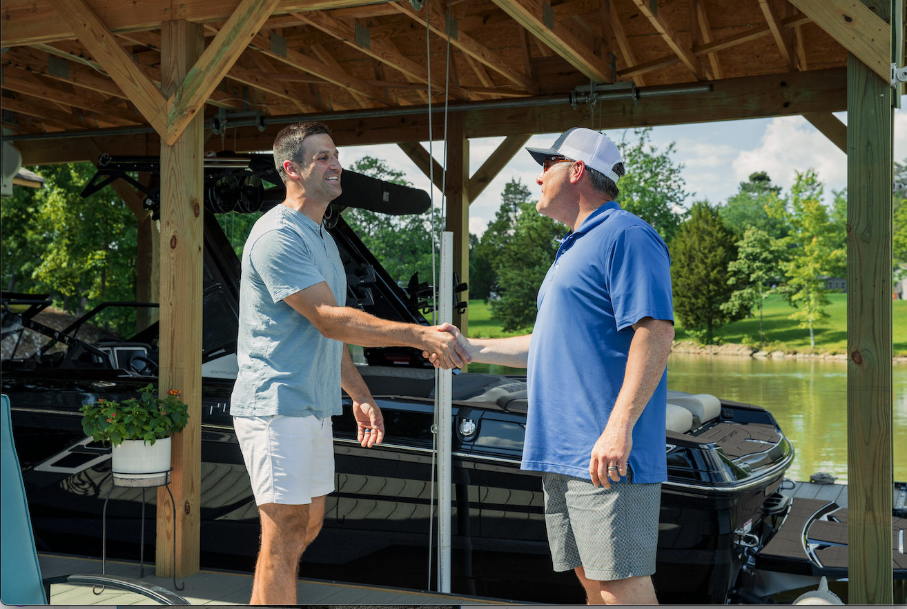Two men are shaking hands in front of a boat.